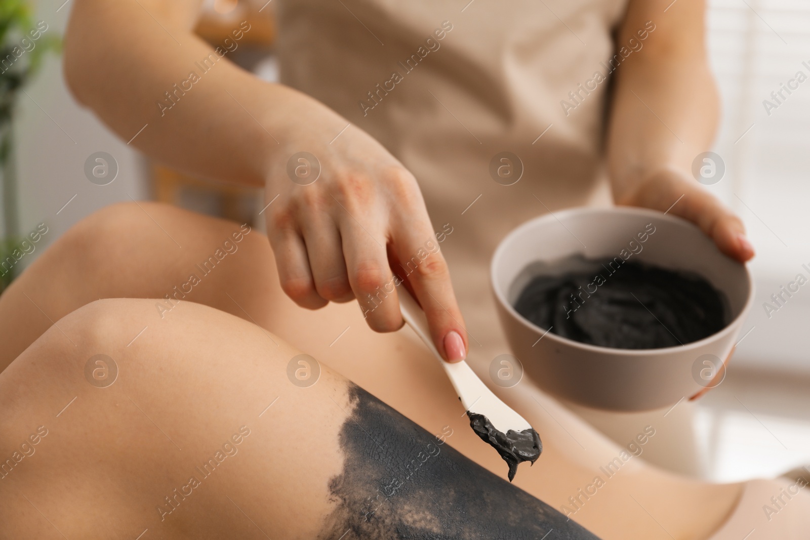 Photo of Esthetician applying cosmetic product for body wraps treatment onto woman's leg in spa salon, closeup