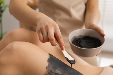 Photo of Esthetician applying cosmetic product for body wraps treatment onto woman's leg in spa salon, closeup