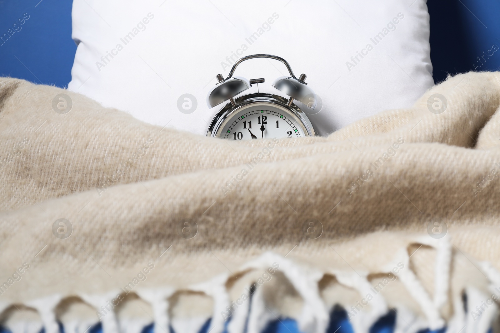 Photo of Alarm clock, pillow and blanket on blue background, closeup. Time for sleeping