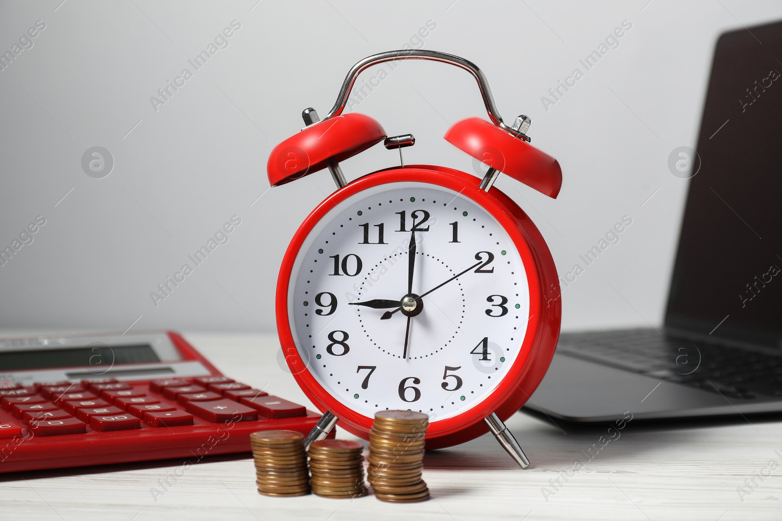 Photo of Alarm clock, coins, laptop and calculator on white wooden table. Tax time