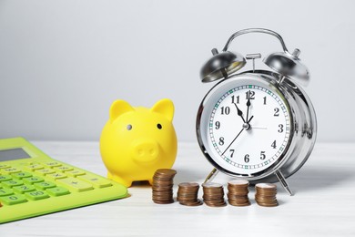 Photo of Alarm clock, coins, calculator and piggy bank on white wooden table. Tax time