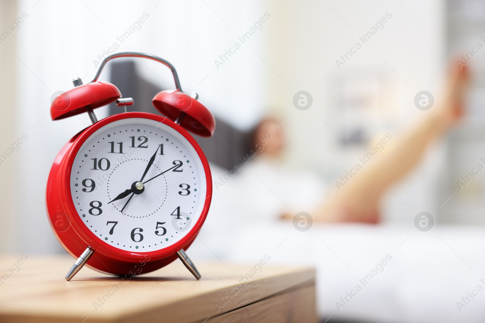 Photo of Young woman exercising on bed at home, focus on alarm clock. Morning routine