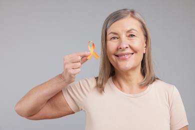 Photo of Multiple Sclerosis awareness. Woman with orange ribbon on light grey background