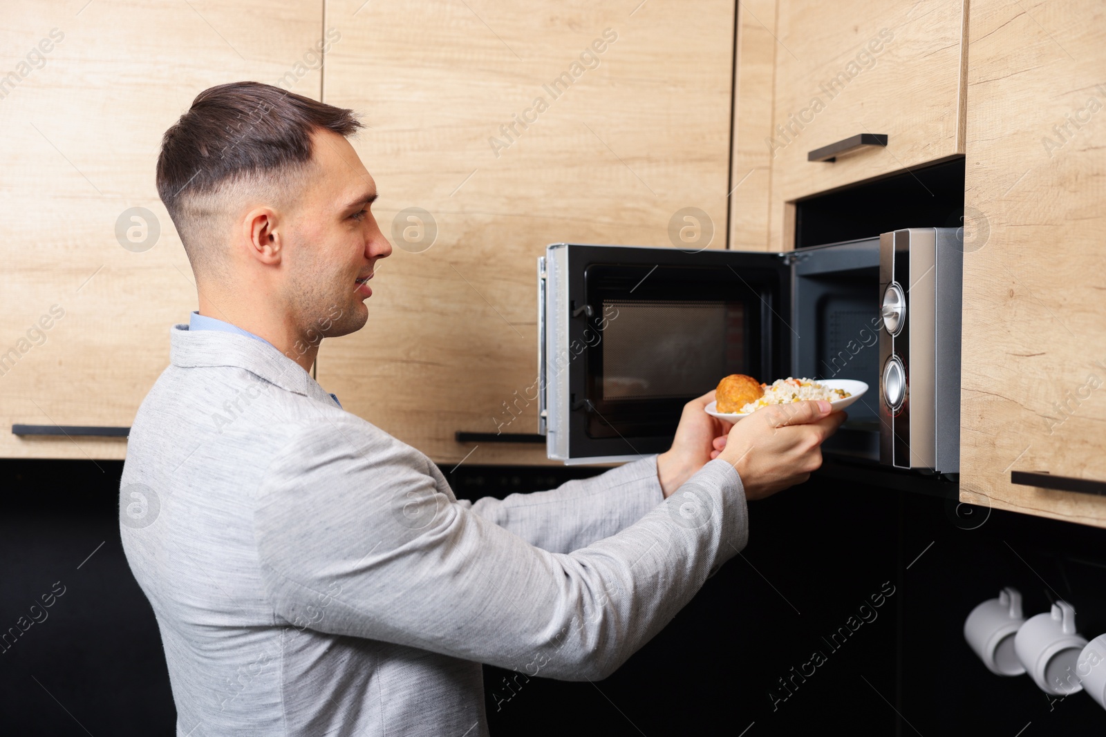 Photo of Man putting plate with lunch into microwave in kitchen