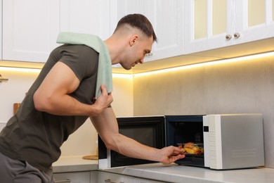 Photo of Man putting container with lunch into microwave in kitchen