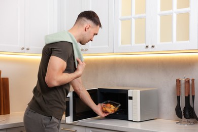 Photo of Man putting container with lunch into microwave in kitchen