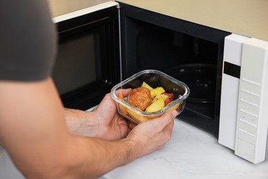 Man putting container with lunch into microwave in kitchen, closeup