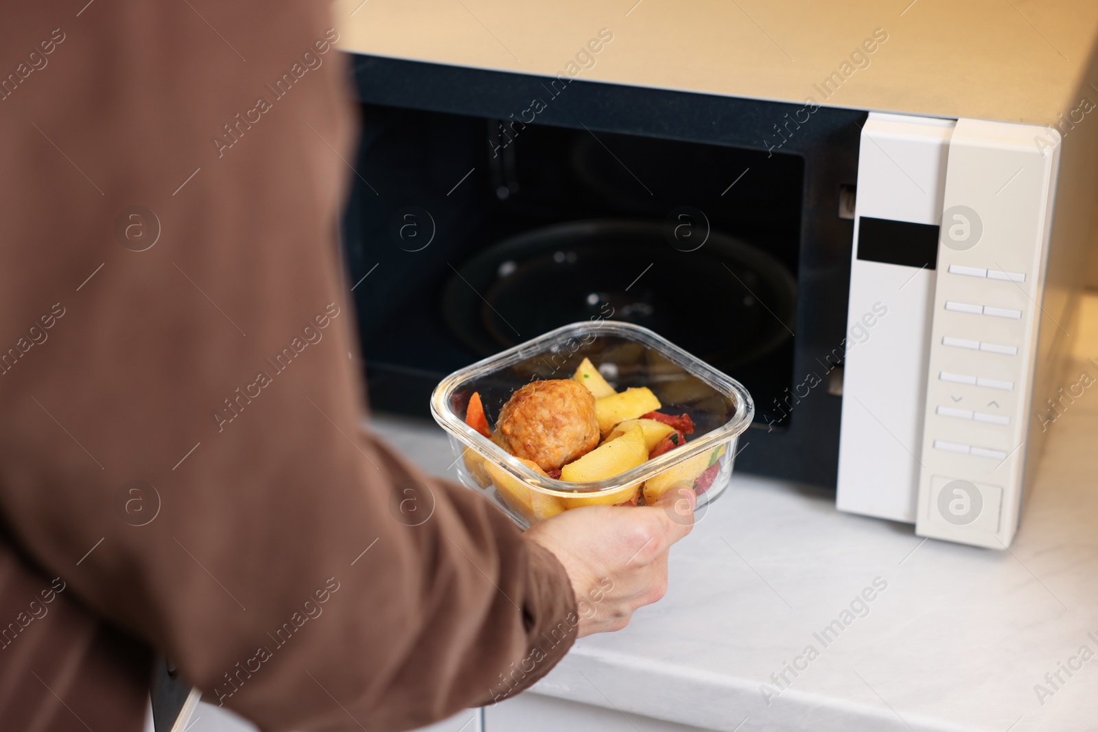 Photo of Man putting container with lunch into microwave in kitchen, closeup