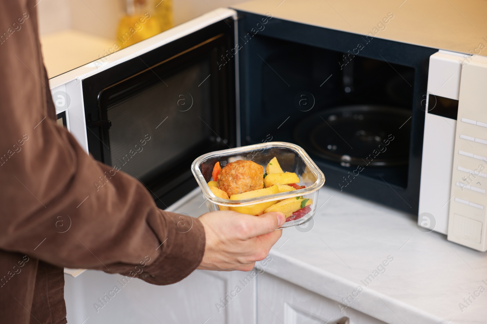 Photo of Man putting container with lunch into microwave in kitchen, closeup