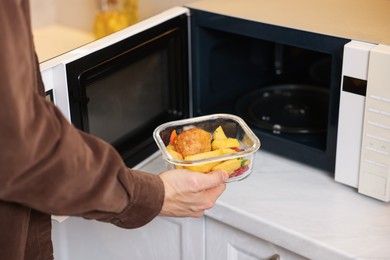 Man putting container with lunch into microwave in kitchen, closeup