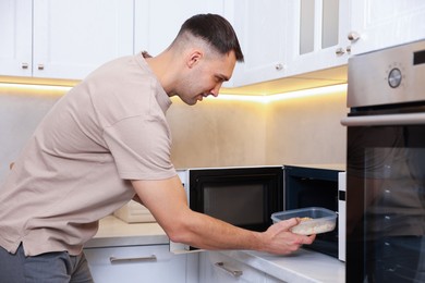 Photo of Man putting container with lunch into microwave in kitchen