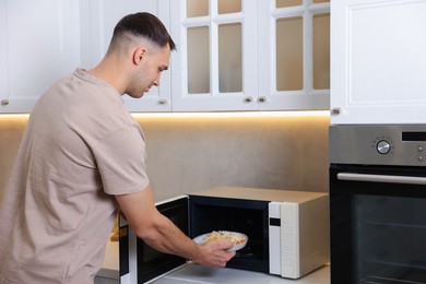 Photo of Man putting plate with lunch into microwave in kitchen