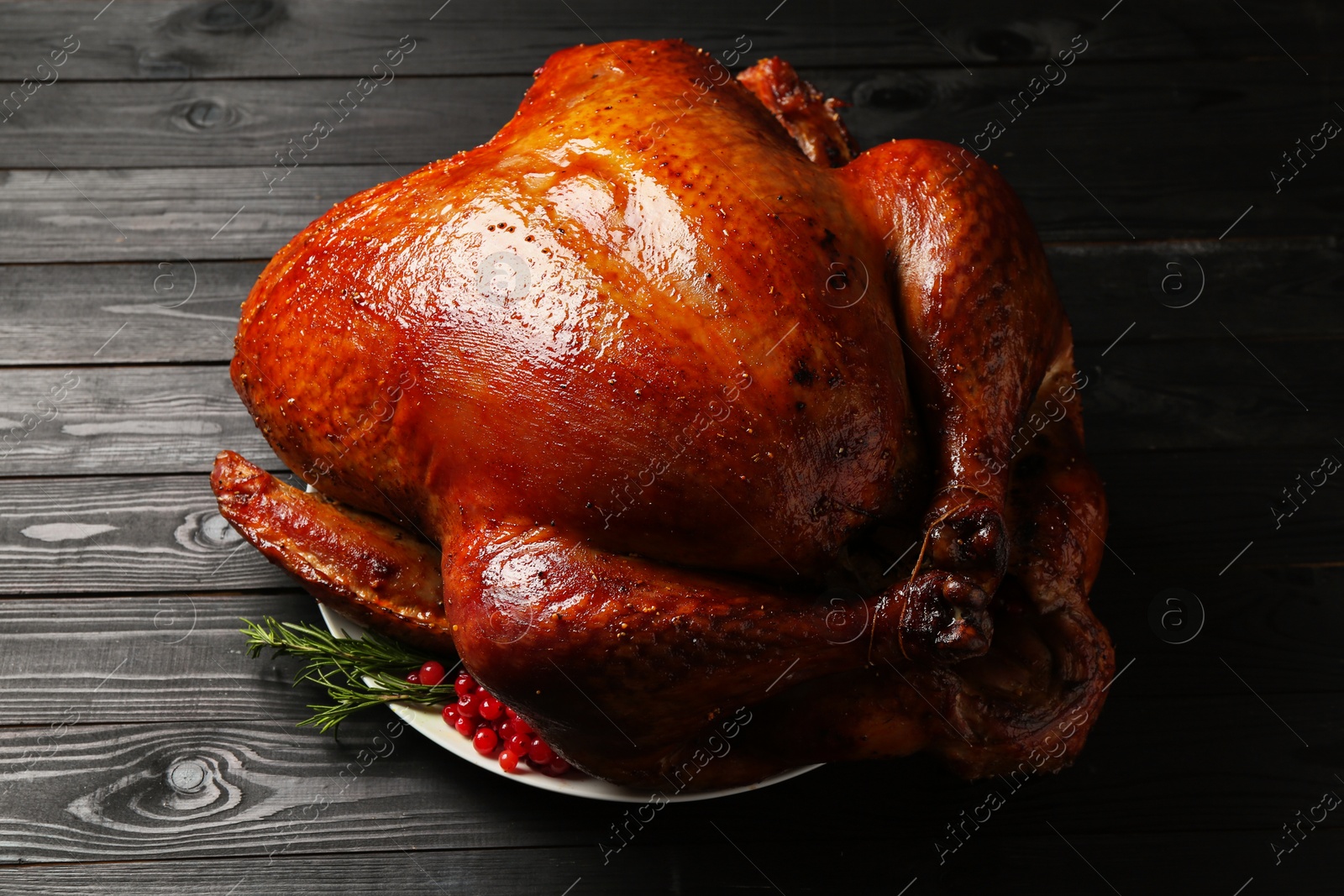 Photo of Whole baked turkey with cranberries and rosemary on black wooden table, closeup