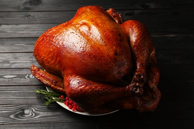 Whole baked turkey with cranberries and rosemary on black wooden table, closeup