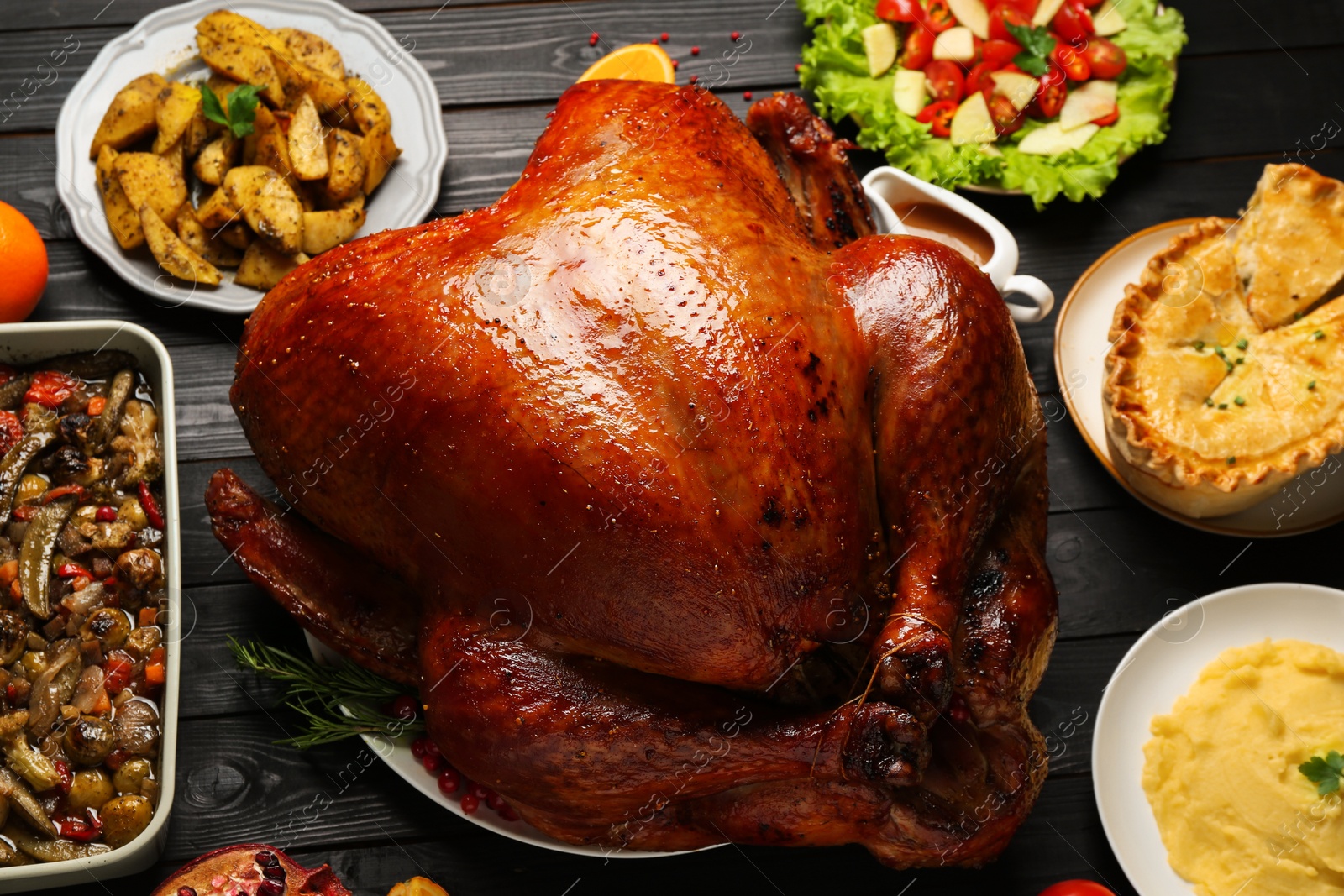 Photo of Whole baked turkey and other dishes served on black wooden table, flat lay