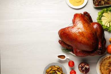 Whole baked turkey and other dishes served on light wooden table, flat lay. Space for text