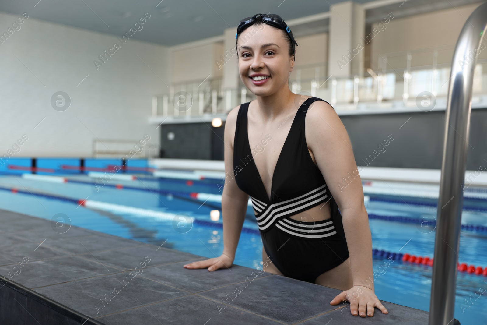 Photo of Happy woman wearing goggles and swimsuit in swimming pool indoors, space for text