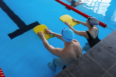 Photo of Young man and woman with kickboards swimming in pool indoors