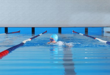 Photo of Young man in cap and goggles swimming in pool indoors