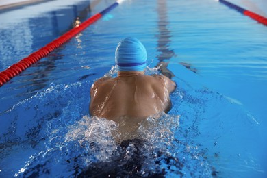 Photo of Young man in cap and goggles swimming in pool indoors, back view