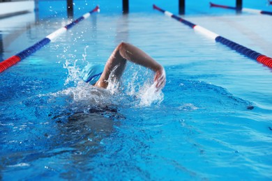 Young man in cap and goggles swimming in pool indoors