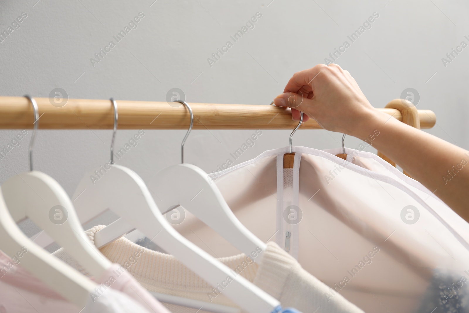 Photo of Woman taking garment cover with clothes from rack indoors, closeup