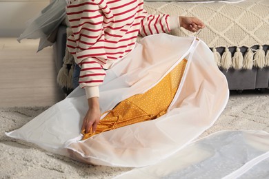 Woman putting clothes into garment cover on floor indoors, closeup