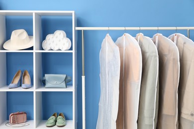 Garment covers with clothes on rack and different accessories near blue wall indoors