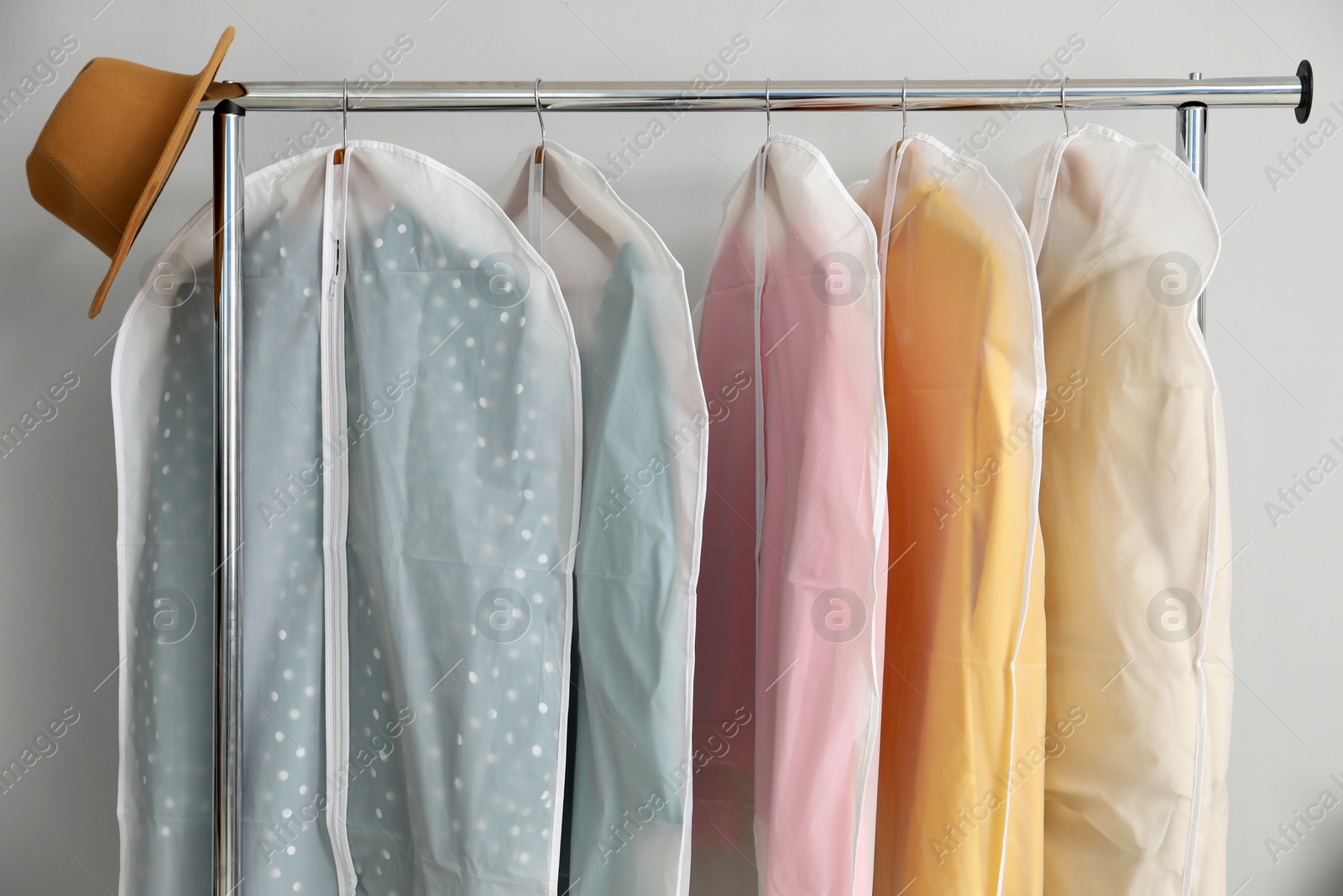 Photo of Garment covers with clothes and hat on rack near grey wall indoors