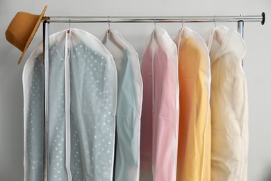 Garment covers with clothes and hat on rack near grey wall indoors