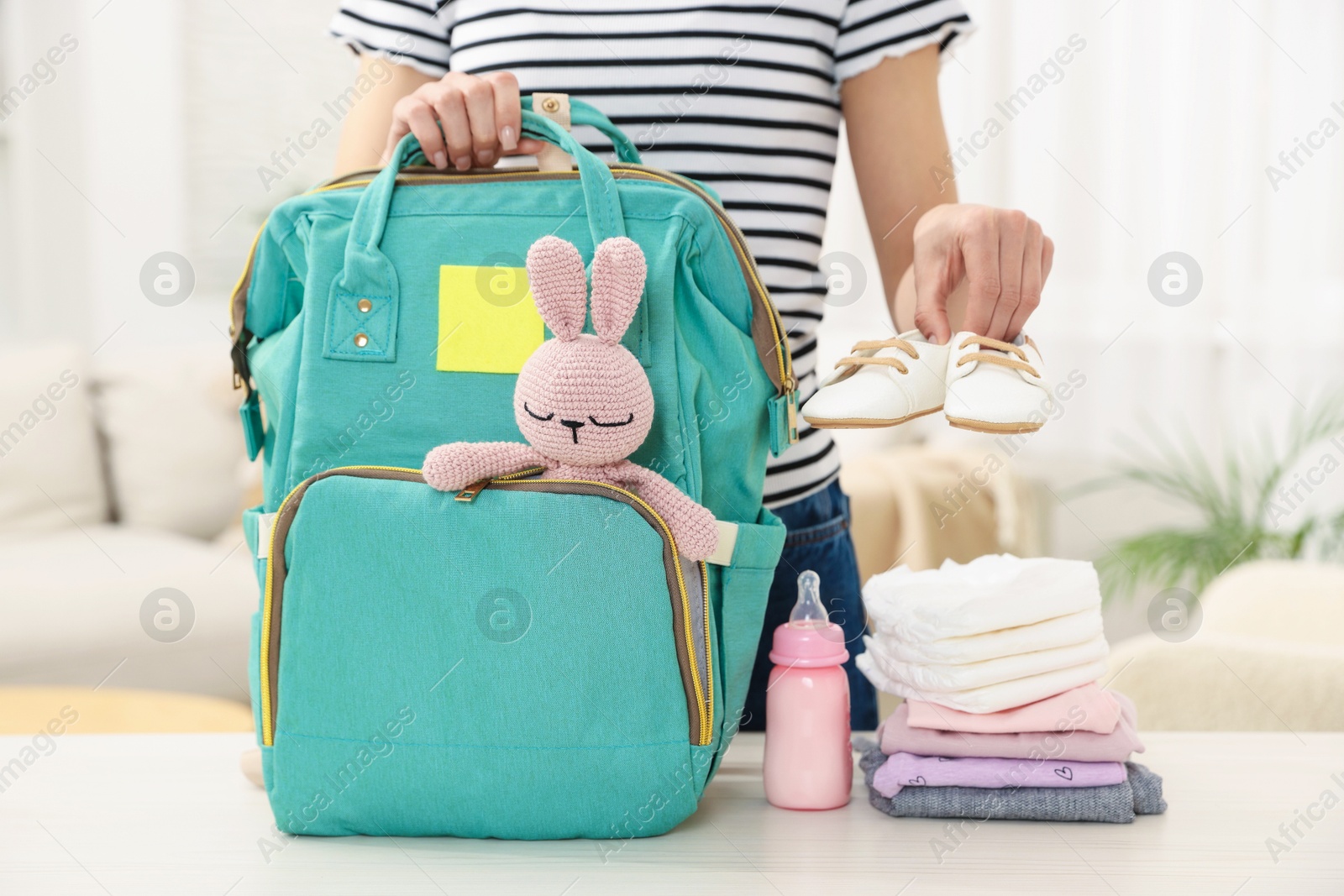 Photo of Mother packing baby's stuff into bag at white table, closeup