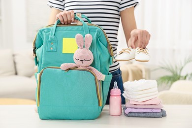 Photo of Mother packing baby's stuff into bag at white table, closeup