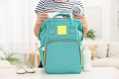 Photo of Mother packing baby's stuff into bag at white table, closeup