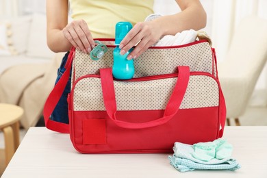 Photo of Mother packing baby's stuff into bag at white table, closeup