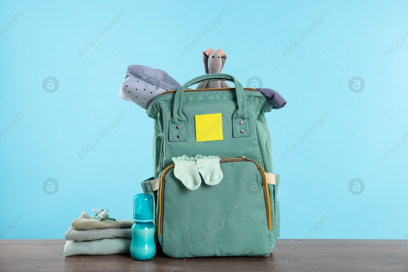 Photo of Mother's bag with baby's stuff on wooden table against light blue background