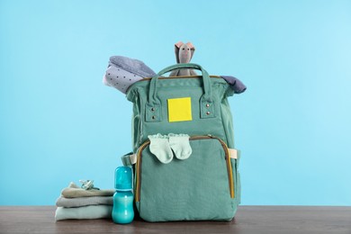 Mother's bag with baby's stuff on wooden table against light blue background