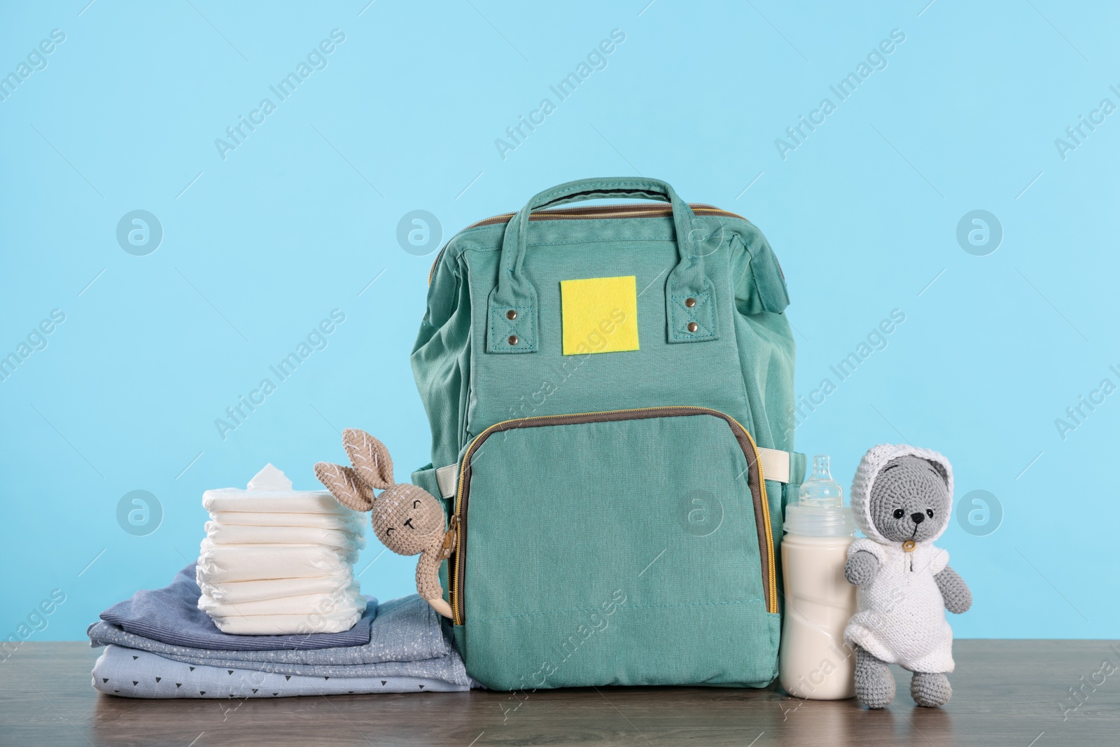 Photo of Mother's bag with baby's stuff on wooden table against light blue background