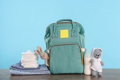 Photo of Mother's bag with baby's stuff on wooden table against light blue background