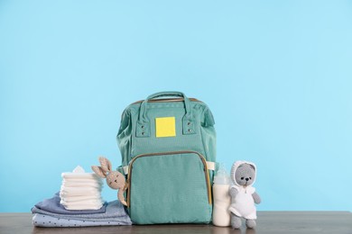 Photo of Mother's bag with baby's stuff on wooden table against light blue background