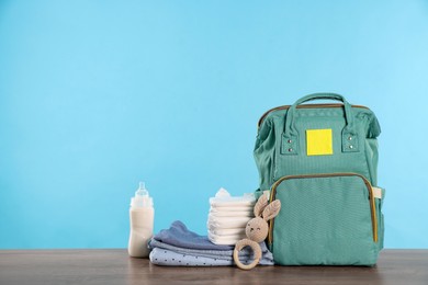 Photo of Mother's bag with baby's stuff on wooden table against light blue background. Space for text