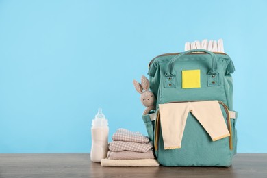 Photo of Mother's bag with baby's stuff on wooden table against light blue background. Space for text