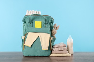 Mother's bag with baby's stuff on wooden table against light blue background