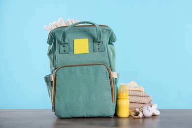 Photo of Mother's bag with baby's stuff on wooden table against light blue background