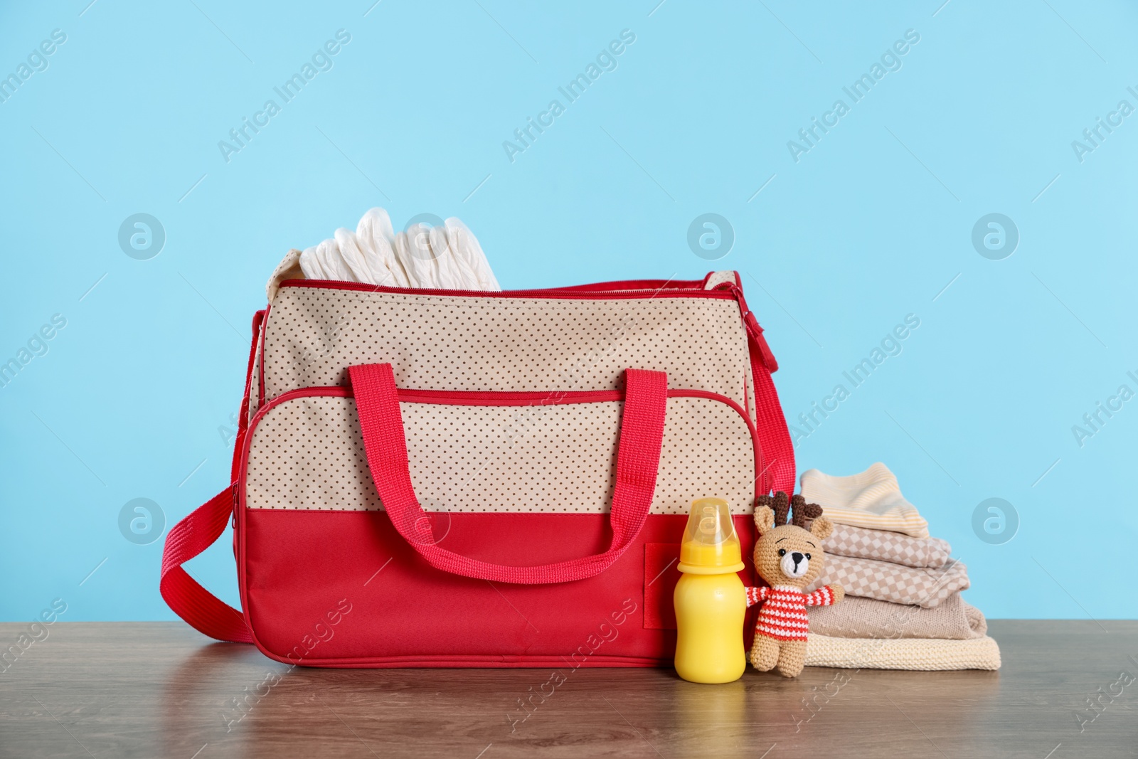 Photo of Mother's bag with baby's stuff on wooden table against light blue background