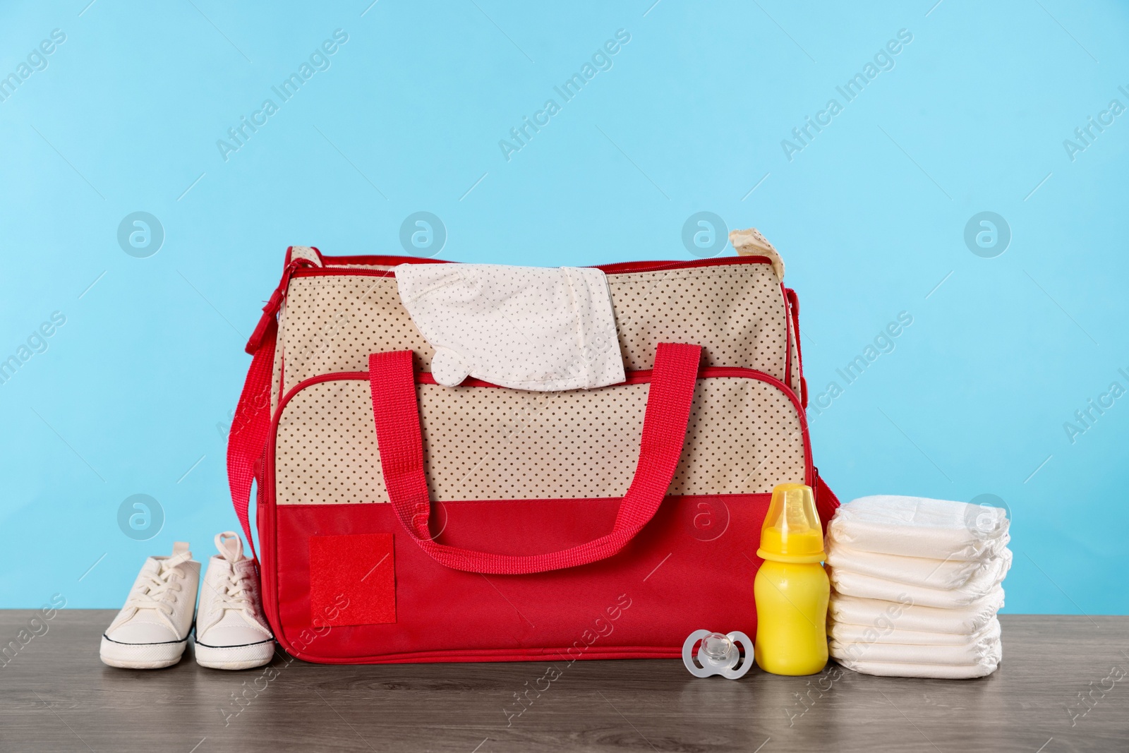 Photo of Mother's bag with baby's stuff on wooden table against light blue background