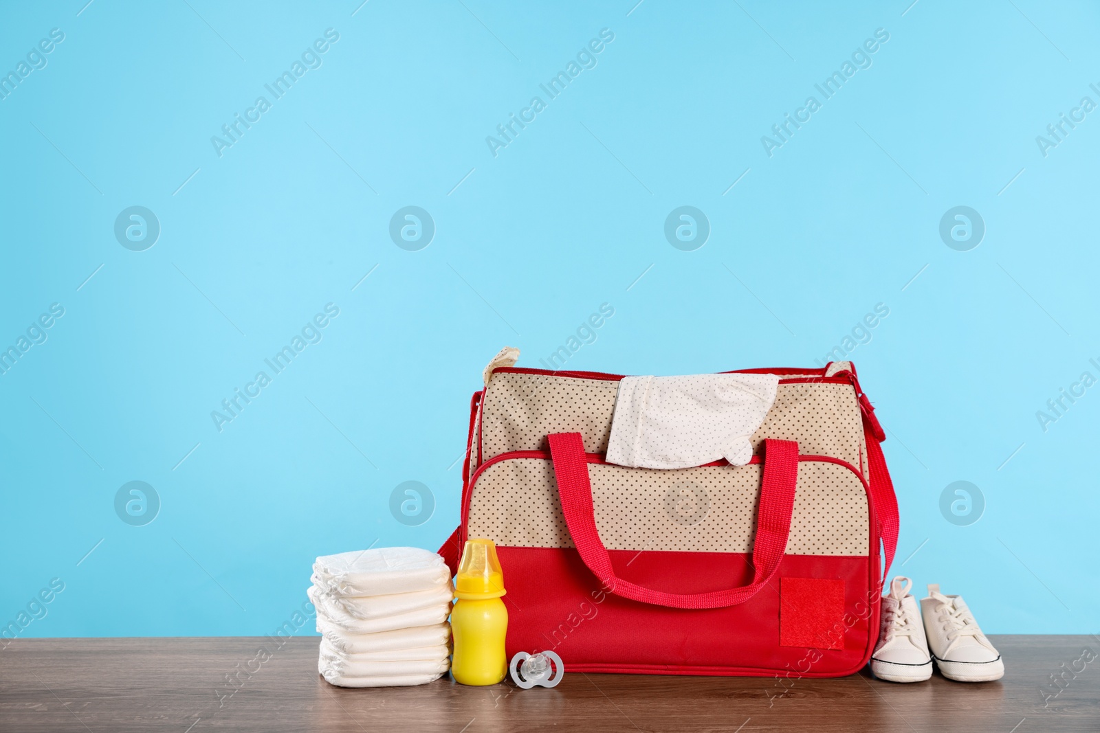 Photo of Mother's bag with baby's stuff on wooden table against light blue background. Space for text