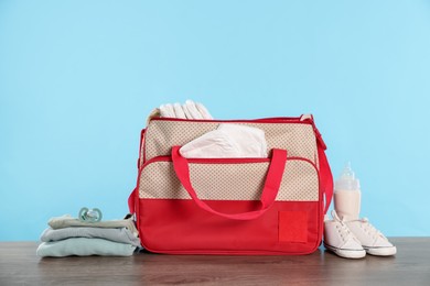 Photo of Mother's bag with baby's stuff on wooden table against light blue background