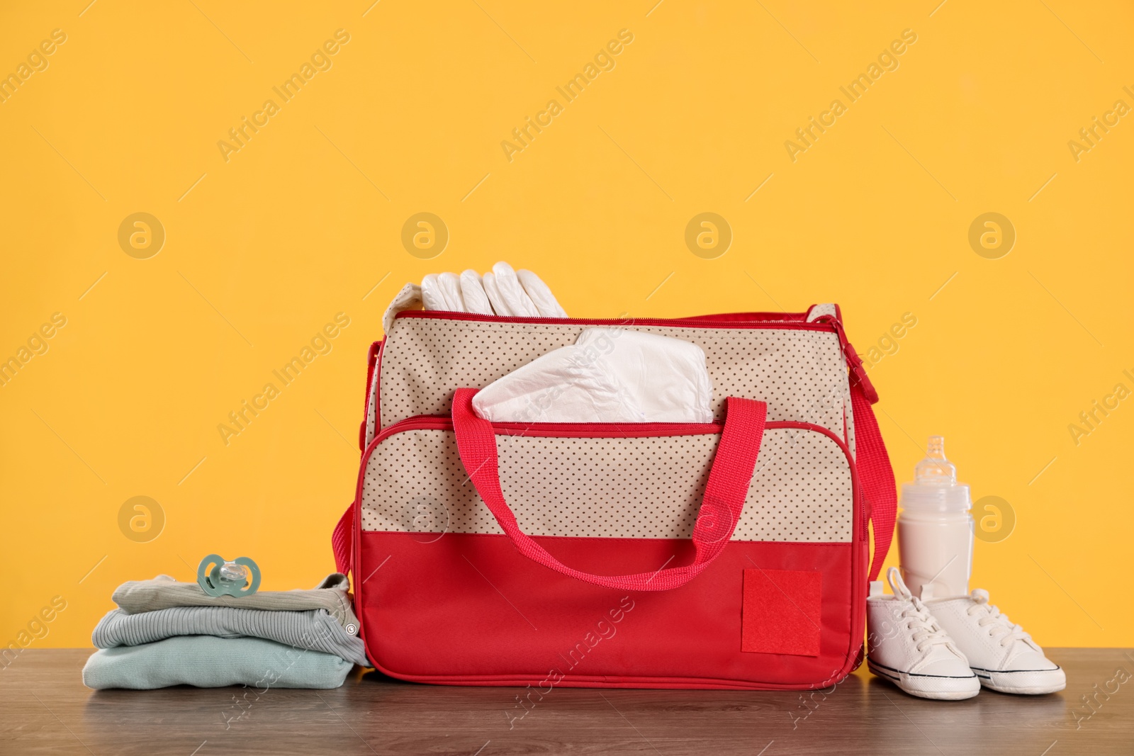 Photo of Mother's bag with baby's stuff on wooden table against orange background