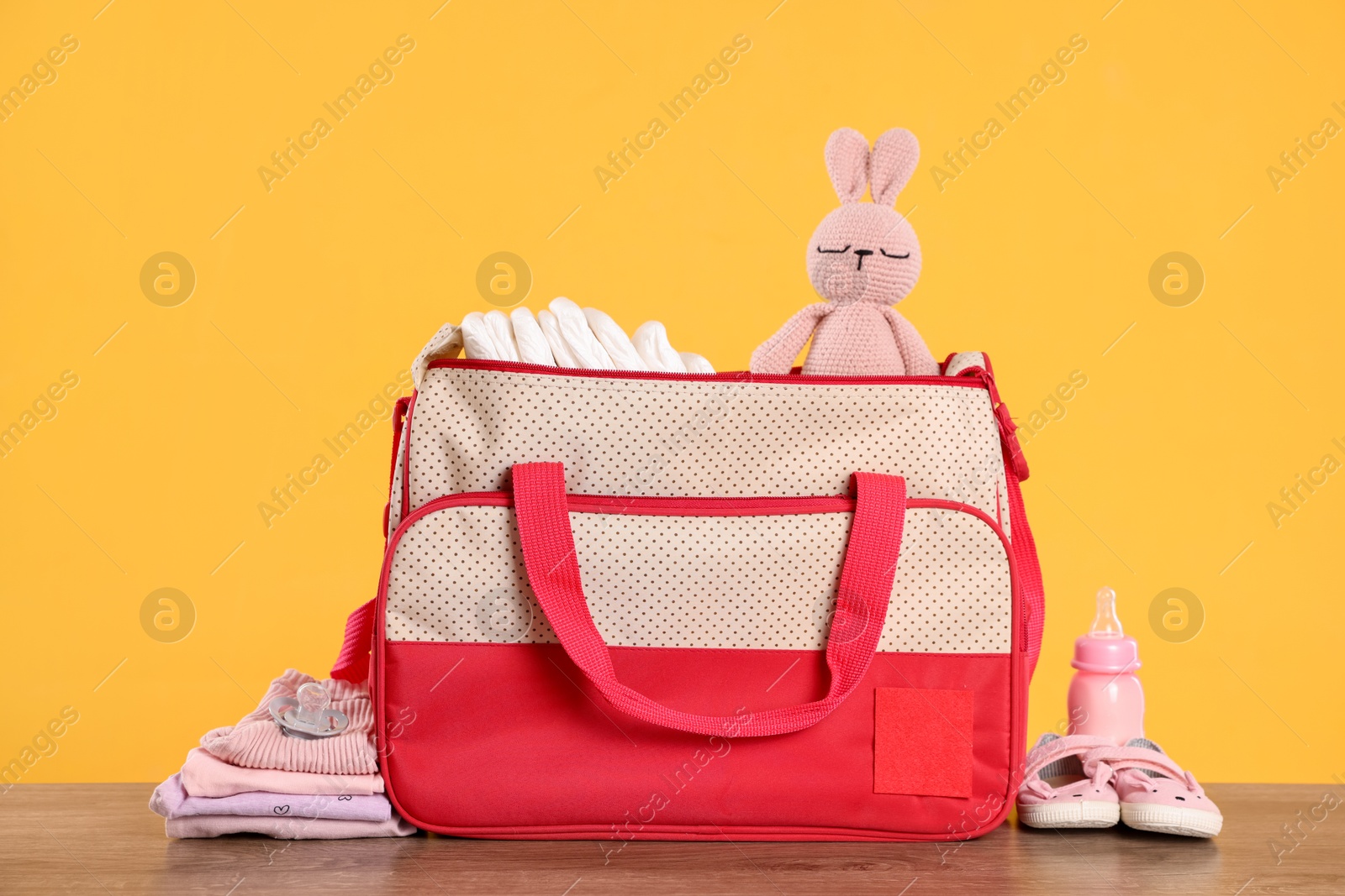 Photo of Mother's bag with baby's stuff on wooden table against orange background