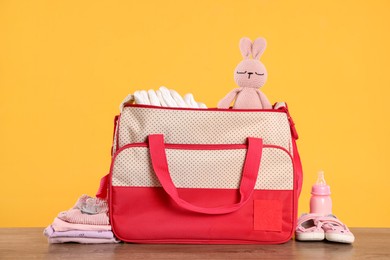 Photo of Mother's bag with baby's stuff on wooden table against orange background